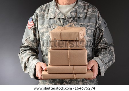 Closeup of a soldier wearing camouflage fatigues holding a stack of packages for mail call. Horizontal format, man is unrecognizable.