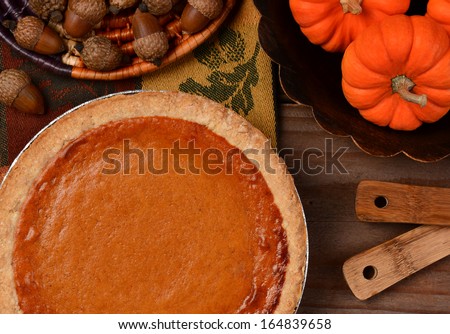 Overhead view of a fresh baked pumpkin pie ready for Thanksgiving. The pie is surrounded by autumn accessories including acorns, and mini pumpkins. Horizontal format.