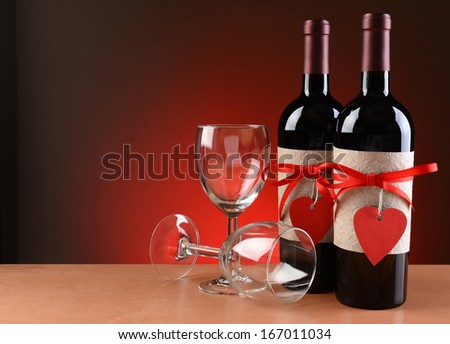 Closeup of a wine bottles decorated for Valentines Day. Two empty wineglasses are next to the bottles with one on its side.  Both bottles have a red ribbon and heart shaped tag and a blank label.