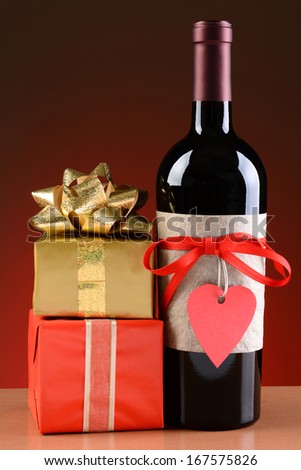 Closeup of a wine bottle decorated for Valentines Day. A stack of presents are next to the bottle. The bottle has a red ribbon and heart shaped tag and a blank label.