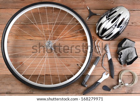 Overhead view of bicycle gear laid out on a rustic wooden floor. Items include, Wheel, pump, gloves, tools, helmet and lock. Horizontal format.