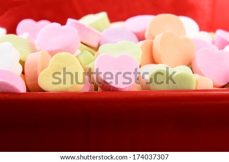 Closeup of assorted pastel candy hearts for Valentines Day in a red ceramic candy bowl. Shallow depth of field. The candies are blank and ready for you to add your own message.