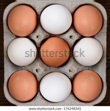 High angle view of a carton of brown and white farm fresh eggs. The nine egg cardboard crate fills the frame with a bit of wood table showing on the sides.