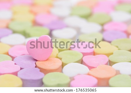 Closeup of a pink candy heart for Valentines Day standing out in a field of out of focus similar candies. Heart is set to one side leaving room for your copy. The candies are blank.