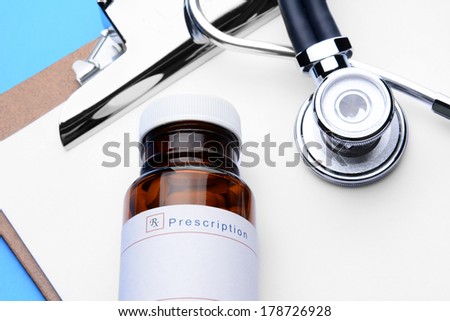 Closeup of a Prescription Bottle, Clipboard and Stethoscope on a clip board with blank paper. Horizontal format with a blue background.