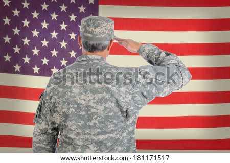 Closeup of a middle aged American soldier in fatigues saluting an old and weathered flag. The flag fills the frame and is out of focus. Man is seen from behind.