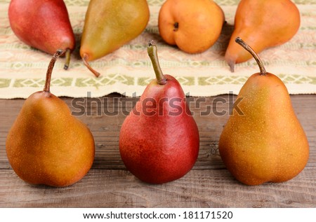 Closeup shot of a group of three pears on a rustic kitchen table. Four out of focus pears lay on a table cloth in the background. Bosc and Red Pears are shown.