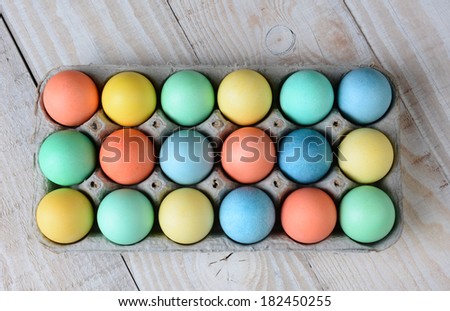 Overhead view of dyed Easter egg carton on a rustic farmhouse kitchen table. Horizontal format.