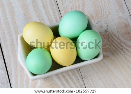 High angle view of a rectangular bowl of pastel Easter eggs on a rustic farmhouse style kitchen table.