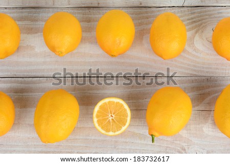 High angle shot of two rows of whole lemons filling the frame with one cut piece of fruit. Horizontal format or a rustic farmhouse style table.