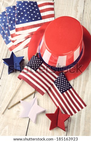 High angle shot of assorted items to celebrate the Fourth of July. Items include, Uncle Sam Hat, American Flags, napkins and red white and blue decorative stars. Vertical format with a vintage look.