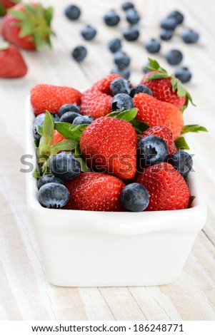 A bowl full of strawberries and blueberries on a rustic farmhouse style kitchen table. Vertical format with shallow depth of field.