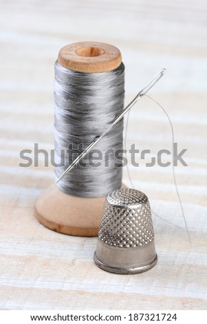 Closeup of an antique thimble and thread spool. A needle sticks through the thread on an old fashioned wooden spool.