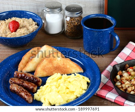 A country style scrambled egg breakfast on a rustic wooden restaurant table. Eggs, sausage links, toast, oatmeal, potatoes, coffee and menu are just some of the items on the table.