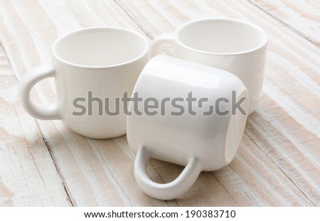 Three white mugs on a rustic whitewashed wood table. Still life study of white on white. Horizontal format.