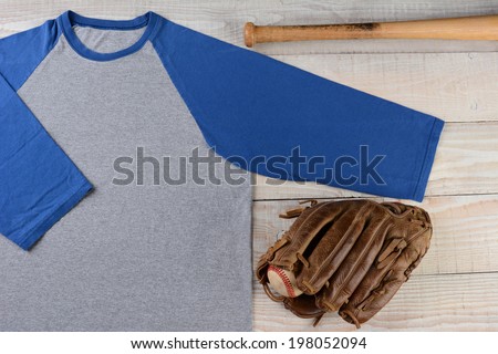 High angle shot of a Baseball jersey with a ball and glove and bat on wooden surface.