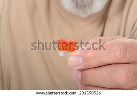 Closeup of a technician holding a fuse in his finger tips. The man is unrecognizable, with shallow depth of field, focus in on the fuse.
