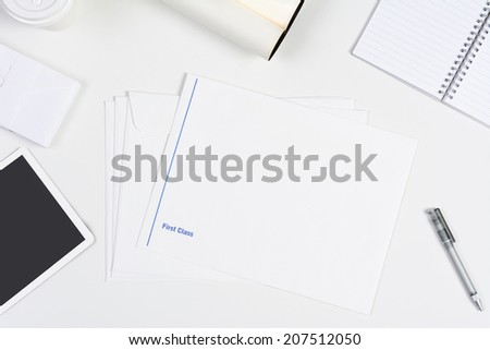 High angle shot of a neat white desk with primarily white office objects. Items include, tablet computer, pad, pens, coffee cup, and envelopes.
