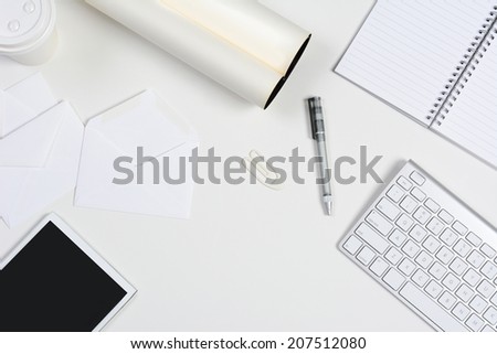 High angle shot of a neat white desk with primarily white office objects. Items include, a tablet computer, keyboard, pad, pen, coffee cup, and envelopes. With copy space.