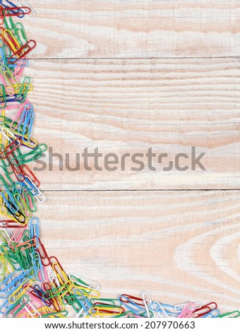 Paper clips in a random pattern on two sides of the image. A whitewashed wood background with multi colored paper clips.