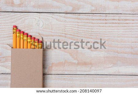 High angle shot of a cardboard box of new pencils on a whitewashed wood desk. The box is set ot the right leaving lots of copy space. Ideal for Back to School projects.