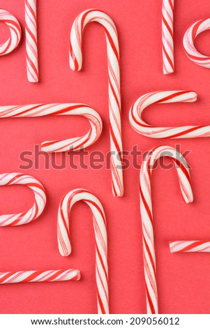High angle shot of a group of Christmas candy canes on a red background. The peppermint sticks run in all directions and out of the frame.