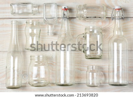 High angle shot of assorted glass bottles on a whitewashed wooden table. Clear glass bottles and containers of various sizes and shapes, horizontal format.