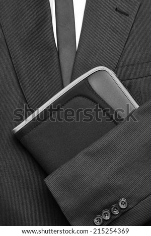 Close up of a man's suit with white shirt and tie and the jacket arm folded over a small notebook. Vertical format in black and white.