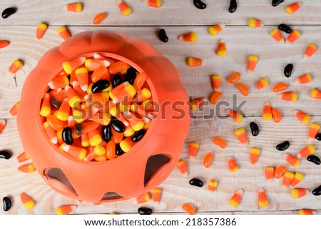 High angle shot of a plastic halloween pumpkin filled with candy on a white rustic wood table. Horizontal format with candy corn and jelly beans scattered on the surface.