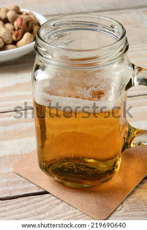 Closeup of a jar mug with beer. Vertical format on a rustic wood table and peanuts in the background.