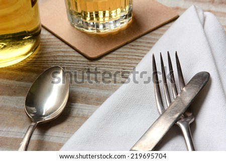 Closeup of a table setting. Old silverware, napkin and drinks on a white wood table. Horizontal format.