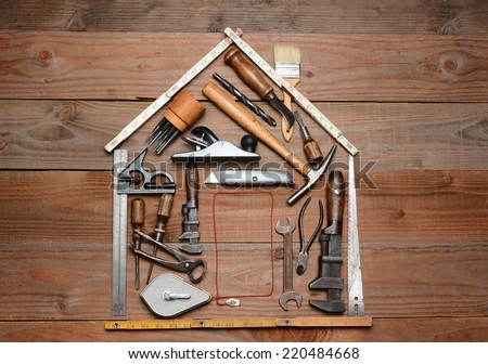 High angle shot of a group of construction tools arranged in the shape of a house. Horizontal format on a rustic wood background.