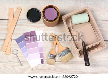 High angle shot of equipment laid out in preparation to paint. Items include: an open paint can, paint, roller, brushes, chip chart, stirrers, opener and tray.