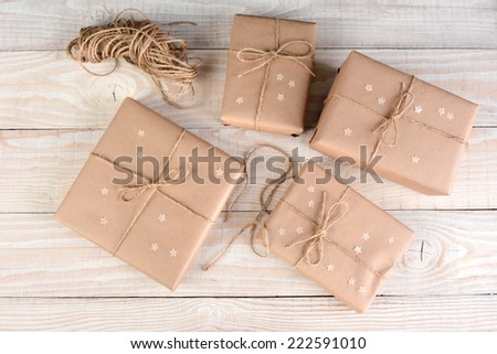 High angle image of four brown packages wrapped with plain brown paper on a white rustic wood table. Paper stars on the boxes that are tied with twine.