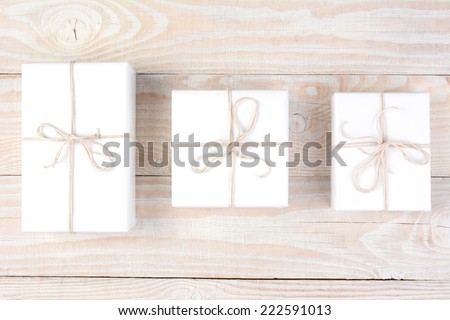 High angle shot of three packages wrapped in plain white paper and tied with white string. Horizontal format on a whitewashed wood table.