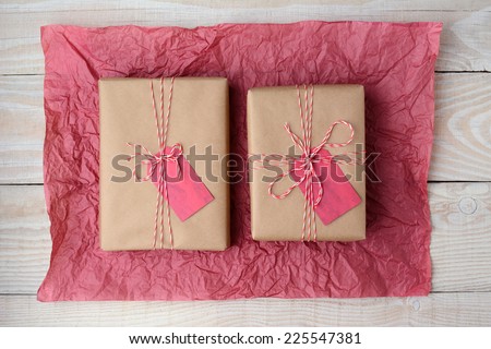 High angle shot of two plain brown paper wrapped presents on a crumpled sheet of red tissue paper. Horizontal format on a rustic white wood table.