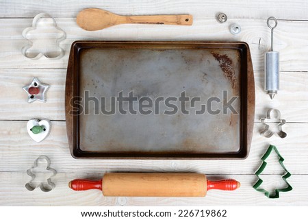 Overhead shot of a group of items for baking Christmas Cookies surrounding an empty cookie sheet. Horizontal format on a  rustic wood kitchen table.