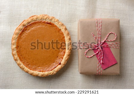 High angle shot of a holiday pumpkin pie and plain paper wrapped present. The brown gift is tied with red and white string and has a red gift tag. Horizontal format.