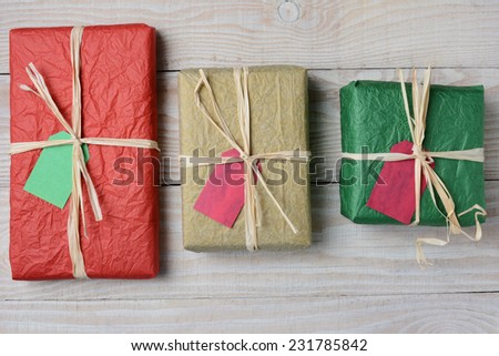 High angle image of three tissue paper wrapped Christmas presents. Horizontal format on a whitewashed rustic wood table.