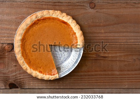 A pumpkin pie with a slice cut out. Horizontal format on a rustic wood table.