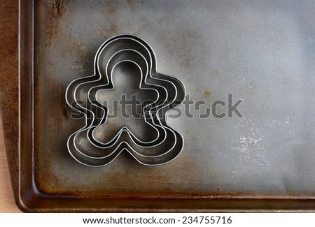 Overhead closeup of gingerbread men cookie cutters on a well used baking sheet. Horizontal format with copy space. Strong sidelight.