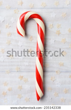 High angle shot of an old fashioned Candy Cane on parchment paper surrounded by tiny paper stars. Vertical format.