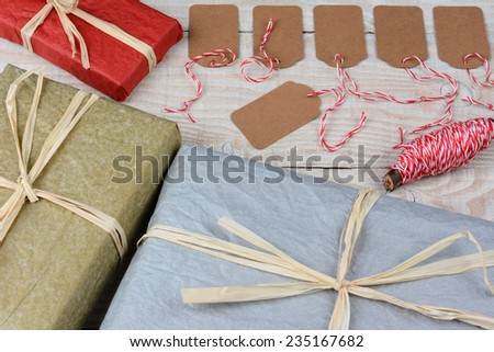 Overhead shot of a group of blank gift tags surrounded by wrapped Christmas presents on a white rustic table. Horizontal format with focus on the gift tags.