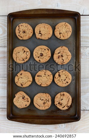 High angle shot of a dozen chocolate chip cookies on a metal baking sheet. Vertical format on a rustic white kitchen table.