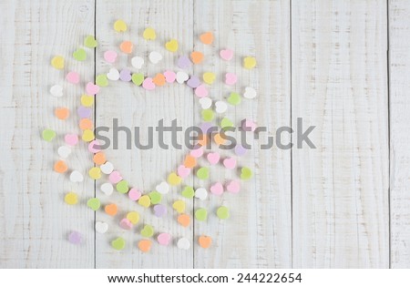 High angle shot of a  group of pastel candy Valentine\'s hearts forming a larger heart shape on a rustic white wood table. Horizontal format with copy space on a white wood table..