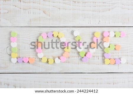 The word LOVE spelled out using pastel candy Valentine\'s hearts. Overhead shot on a rustic whitewashed wood table with copy space.