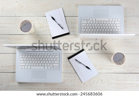 High angle shot of two computer work stations back-to-back with almost identical layouts. Horizontal format on a whitewashed wood table.