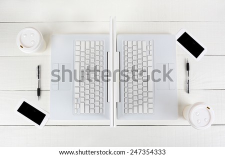 High angle shot of two laptop work stations back-to-back with mirror image identical layouts. Horizontal format on a white wood table.