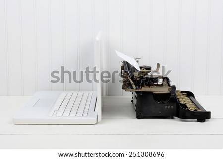 Closeup of a white desk with a modern laptop computer and an antique typewriter back to back. Horizontal format with copy space. Old vs new concept.