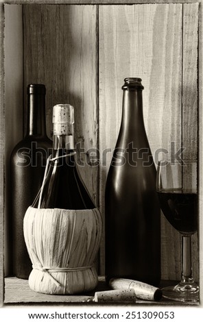 A wine still life with warm light from a window on the side. Three bottles, a wine glass and cork screw in a rustic setting, Vertical format. Vintage effect added.